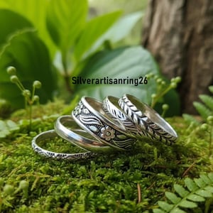 May include: A collection of silver rings with intricate floral and leaf patterns. The rings are displayed on a bed of green moss, with the text "Silverartisanring26" visible in the background. The rings vary in design, showcasing detailed craftsmanship.