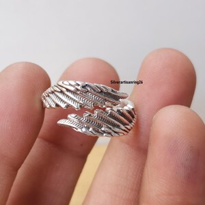 May include: A silver-colored ring with a feather design. The ring wraps around the finger with detailed feather textures. The ring is shown against a neutral background. The text "Silverartisanring26" is visible.