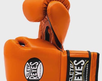 May include: A pair of orange boxing gloves. The gloves are made of leather and feature the "CLETO REYES" logo in white and black. The gloves are designed for professional use.