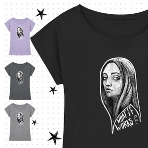 Könnte beinhalten: Schwarzes T-Shirt mit einer weißen Illustration eines Frauengesichts und dem Text "WHAT IF WORKS?". Zusätzliche T-Shirts in Grau und Lavendel sind ebenfalls zu sehen, jedes mit dem gleichen Design. Die Shirts haben kurze Ärmel und einen Rundhalsausschnitt.