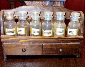 Estante para especias vintage de madera que incluye 6 botellas de vidrio y etiquetas adicionales para especias de estilo rústico campestre. Tiene dos cajones pequeños.