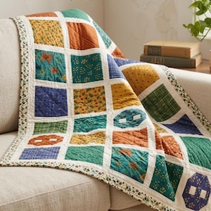 May include: A patchwork quilt featuring a grid of square fabric blocks in various colors including mustard yellow, teal, burnt orange, and navy blue. The blocks display diverse floral, plaid, and dotted patterns, all separated by white sashing.