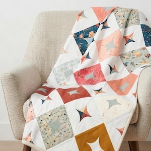 Op de afbeelding: Een quilt met een geometrisch patroon van witte vierkanten afgewisseld met vierkanten in tinten mosterdgeel, koraal, blauwgroen en bloemenprints. Elk vierkant bevat een uitgesneden vierpuntige ster voor een herhalend ontwerp.