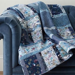 Puede incluir: Una colcha de patchwork que presenta una variedad de cuadrados de tela en tonos azules, blancos y grises. La colcha muestra una mezcla de patrones florales, botánicos y sólidos dispuestos en una cuadrícula, con costuras visibles uniendo cada sección.