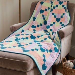 May include: A patchwork quilt featuring a repeating pattern of dark teal hearts interspersed with squares in shades of light pink, pale yellow, and soft lavender. The quilt is finished with a dark teal fabric border along all of its edges.