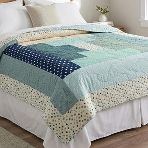 May include: A patchwork quilt featuring a geometric pattern in shades of navy blue, teal, light blue, and cream. The design incorporates various fabric textures, including solid colors, white polka dots on navy, and small dot patterns on cream fabric.