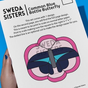 Op de afbeelding: Een wit papier met een Common Blue Bottle Butterfly-ontwerp, tegen een blauwe achtergrond. Het ontwerp toont een roze en blauwe vlinderillustratie. Tekst bevat "SWEDA SISTERS" en instructies voor het afdrukken en schalen van het ontwerp, met een vierkant van 2,54 cm.