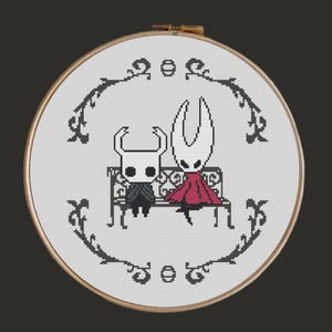 Pode incluir: Um bastidor de bordado em ponto cruz com dois personagens pixelados sentados num banco. Um usa uma capa vermelha, o outro uma roupa escura. O desenho é emoldurado por uma borda preta decorativa sobre um fundo branco.