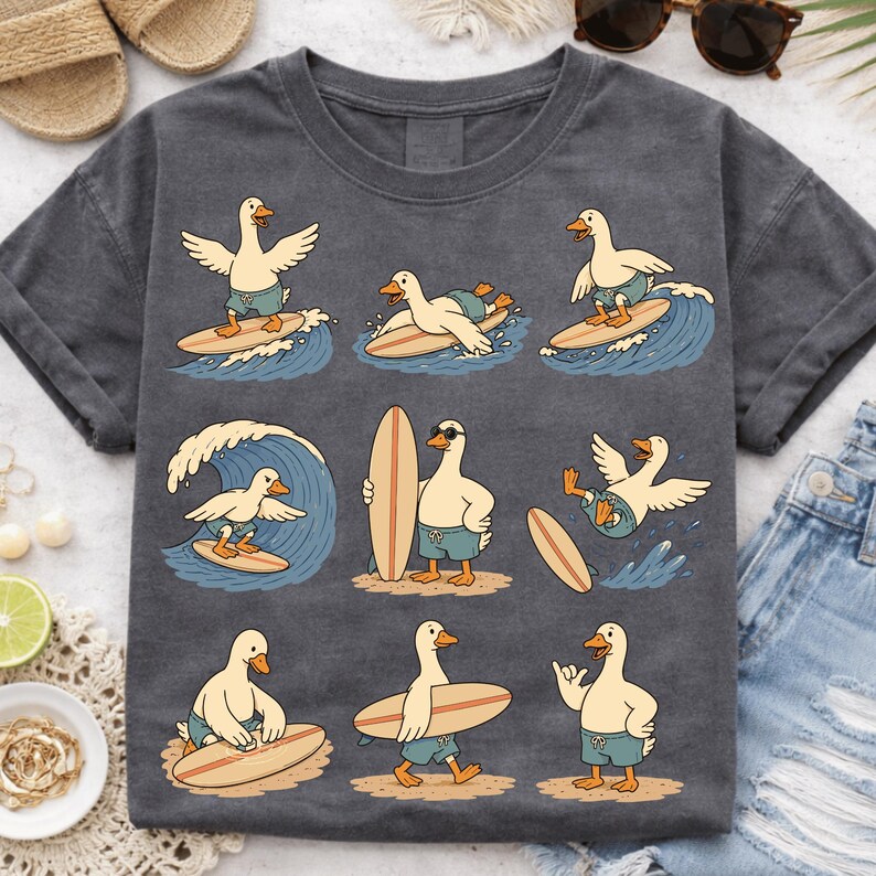 Pode incluir: Uma t-shirt cinzento-carv&atilde;o com uma impress&atilde;o gr&aacute;fica de nove patos de desenhos animados em v&aacute;rias poses de surf. Os patos usam cal&ccedil;&otilde;es de banho azuis, surfam em ondas azuis ou est&atilde;o de p&eacute; em praias de areia com as suas pranchas.