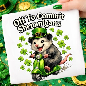 May include: White square with a cartoon opossum riding a green scooter, wearing a green leprechaun hat, and surrounded by shamrocks. Text reads "Off To Commit Shenanigans".