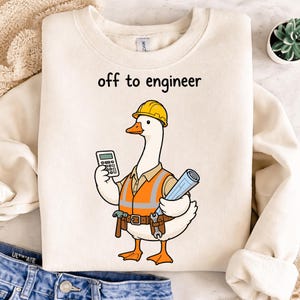 May include: Cream-colored sweatshirt with the text "off to engineer." The graphic features a cartoon goose wearing a yellow hard hat, orange safety vest, and tool belt, holding a calculator and blueprints.