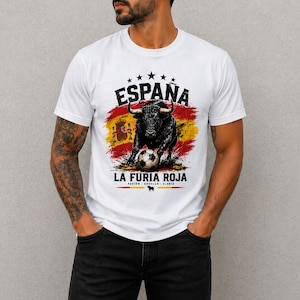 May include: White t-shirt featuring a graphic of a black bull with a soccer ball, the Spanish flag, and the words "España" and "La Furia Roja". The design includes stars and the words "Pasión - Orgullo - Gloria".