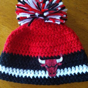 Pode incluir: Bon&eacute; de croch&ecirc; vermelho, preto e branco com um pompom no topo e um logotipo do Chicago Bulls na frente.