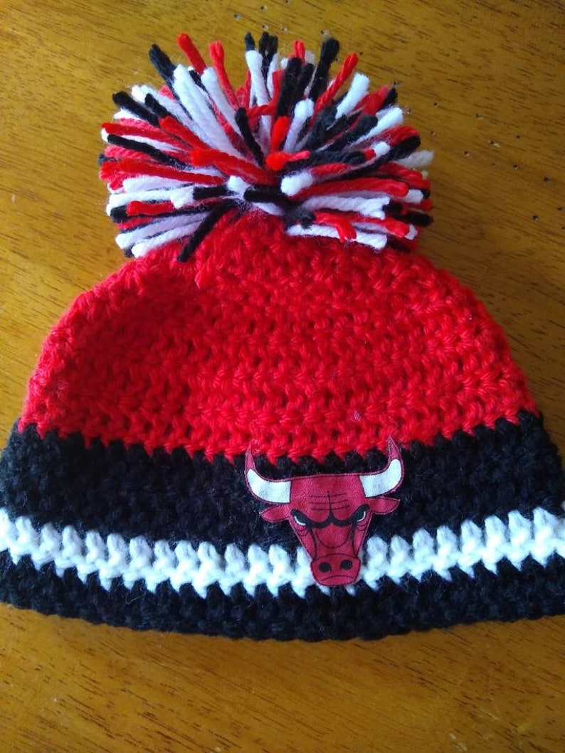 Pode incluir: Bon&eacute; de croch&ecirc; vermelho, preto e branco com um pompom no topo e um logotipo do Chicago Bulls na frente.