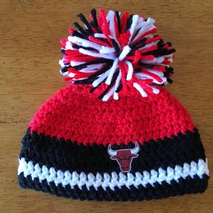 Pode incluir: Bon&eacute; de croch&ecirc; vermelho, preto e branco com um pompom no topo e um patch com o logotipo do Chicago Bulls.