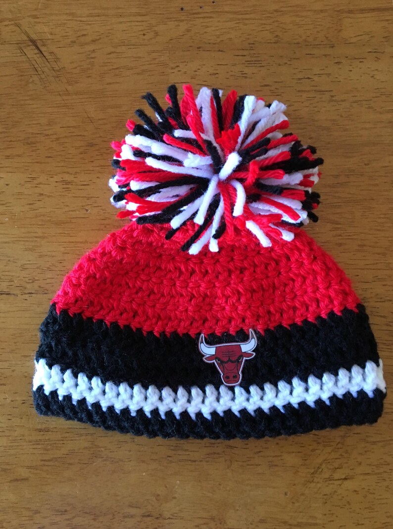 Pode incluir: Bon&eacute; de croch&ecirc; vermelho, preto e branco com um pompom no topo e um patch com o logotipo do Chicago Bulls.