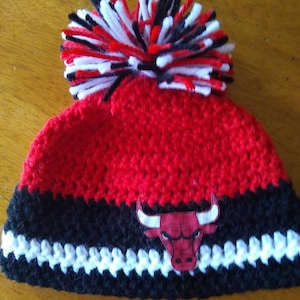 Pode incluir: Boina de croch&ecirc; vermelha e preta com um pompom branco e um logotipo de touro vermelho e preto.