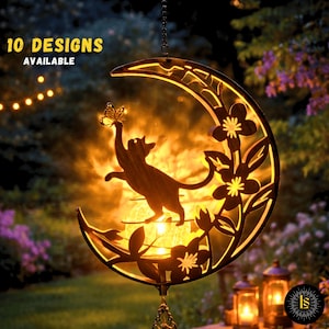 May include: A decorative metal moon-shaped garden ornament with a cat silhouette reaching for a butterfly. The ornament has floral cutouts and is illuminated from within, with the text "10 DESIGNS AVAILABLE" at the top. The background shows a garden setting.