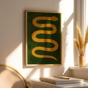 Könnte beinhalten: Ein gerahmter Wandkunstdruck mit einer goldgelben Schlange in einer wellenförmigen, horizontalen S-Form vor einem tiefen waldgrünen Hintergrund. Das Kunstwerk ist in einem dünnen, metallisch goldenen Rahmen gefasst und zeigt eine einfache Grafik.