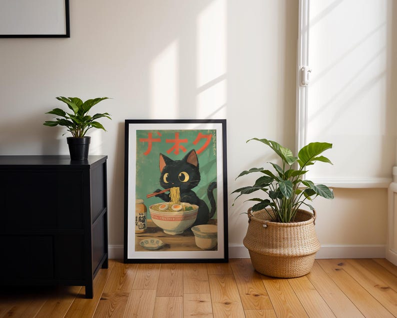 May include: A framed poster featuring a black cat eating ramen noodles. The poster has Japanese text and a green background. The cat is depicted with large eyes and is holding chopsticks. The poster is displayed on a wooden floor next to a black cabinet and a potted plant.