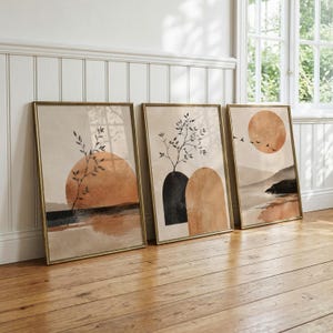 Könnte beinhalten: Drei gerahmte Wandbilder mit abstrakten Landschaften in Beige-, Terrakotta- und Schwarztönen. Die Motive zeigen einen sonnenartigen Kreis, einen belaubten Zweig, bogenförmige Elemente und die Silhouette von Vögeln über einer Horizontlinie.