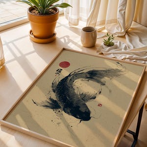 May include: A framed art print featuring a black koi fish in a traditional Japanese ink wash painting style. The artwork includes a red sun and Japanese characters. The print is displayed on a light-colored wooden surface.