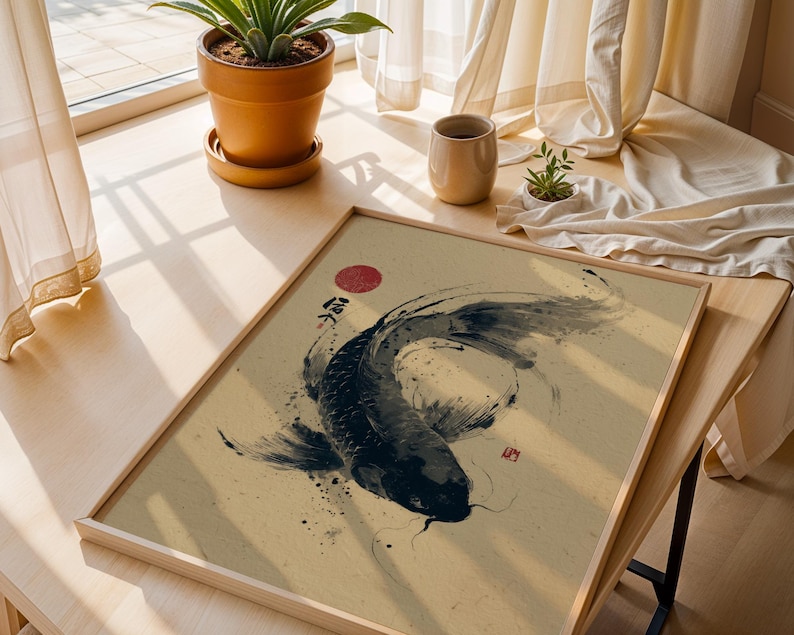 May include: A framed art print featuring a black koi fish in a traditional Japanese ink wash painting style. The artwork includes a red sun and Japanese characters. The print is displayed on a light-colored wooden surface.