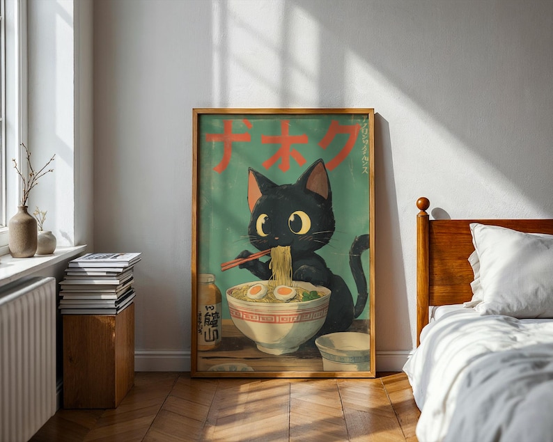 May include: A framed poster featuring a black cat enjoying ramen. The cat, with large yellow eyes, holds chopsticks and eats noodles from a bowl. The poster has Japanese text and a teal background. A bottle of sauce and a small bowl are also visible.