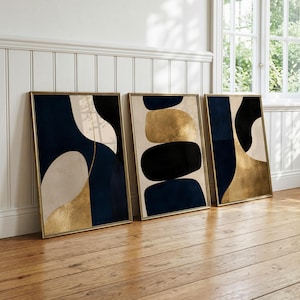 Könnte beinhalten: Drei gerahmte rechteckige Wandbilder mit abstrakten Kompositionen aus organischen Formen in Marineblau, Schwarz, Creme und Metallic-Gold. Jedes Stück ist in einen dünnen Goldrahmen gefasst und zeigt glatte, geschwungene und abgerundete Farbflächen.