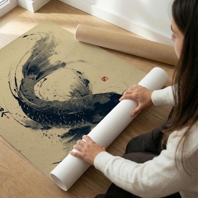 May include: A beige print of a koi fish in the Japanese sumi-e style. The fish is depicted in shades of black and gray with ink splatters. The print is on a beige paper and is rolled up with a white tube.