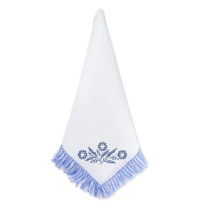 May include: White linen napkin with a blue floral embroidery design and fringed edges. The embroidered design features three stylized flowers and leaves. The napkin is folded into a triangle shape.