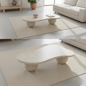 May include: A modern, beige coffee table with a unique, organic shape. The tabletop is supported by two rounded, spherical bases. The table sits on a neutral-toned rug, creating a minimalist aesthetic. The table's dimensions are approximately 47 inches long and 24 inches wide.
