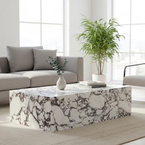 Peut inclure: Une table basse rectangulaire avec une surface blanche effet marbre et des veines marron foncé. La table est dans un salon avec un canapé gris, une plante verte et un vase avec de la verdure. La table mesure environ 122 cm de long.