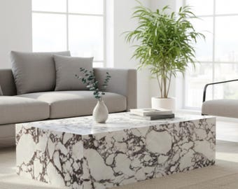 May include: A rectangular coffee table with a white marble-like surface and dark brown veining. The table is in a living room setting with a gray sofa, a green plant, and a vase with greenery. The table measures approximately 48 inches long.