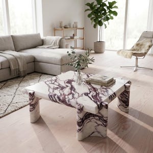May include: Square marble coffee table with a white base and striking purple veining. The table has a unique design with rounded legs and a polished finish. A modern piece for a living room.