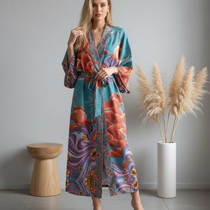 May include: A long, flowing robe with a colorful cloud and floral pattern. The robe features a teal background with orange, purple, and gold accents. It has wide sleeves and a matching belt. The model is wearing beige heels.