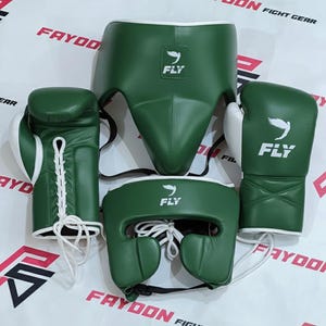 Puede incluir: Un conjunto de equipo de boxeo verde, que incluye guantes, casco y protector inguinal. Los guantes tienen detalles blancos y cordones. El casco y el protector inguinal son verdes con ribetes blancos. La marca "FLY" es visible en cada pieza.
