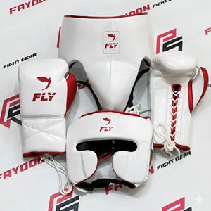Puede incluir: Un juego completo de equipo de boxeo blanco y rojo, que incluye guantes, casco y protector. Cada pieza presenta el logotipo "FLY". Los guantes tienen detalles rojos y cordones blancos. El conjunto está diseñado para boxeo o sparring.