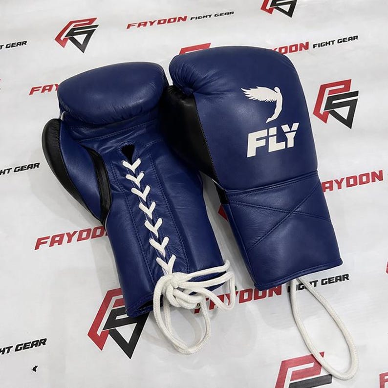 May include: Two navy blue boxing gloves with white laces. The gloves have black detailing and the word "FLY" is printed in white, along with a bird graphic. The brand name "FAYDON FIGHT GEAR" is visible in the background.
