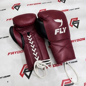 May include: Burgundy boxing gloves with black detailing. The gloves have white laces and the word "FLY" with a wing logo. The text "FAYDOON FIGHT GEAR" is visible in the background.