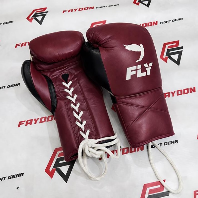 May include: Burgundy boxing gloves with black detailing. The gloves have white laces and the word "FLY" with a wing logo. The text "FAYDOON FIGHT GEAR" is visible in the background.