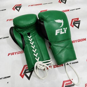 May include: A pair of green boxing gloves with black detailing. The gloves are laced with white cord and feature the word "FLY" with a wing design. The background displays the text "FAYDON FIGHT GEAR".