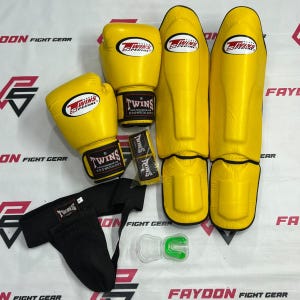 Puede incluir: Un conjunto de equipo de boxeo amarillo Twins Special que incluye dos guantes de boxeo, dos espinilleras, una coquilla negra, un par de vendas amarillas y un protector bucal verde en un estuche de plástico transparente, con el logo Twins Special.