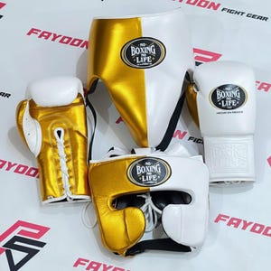 Puede incluir: Equipo de boxeo que incluye guantes dorados y blancos, protector de cabeza y protector inguinal. Los guantes y el protector de cabeza tienen el texto "NO BOXING NO LIFE". Diseñado para entrenamiento y competición de boxeo.