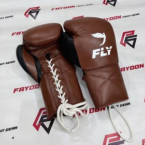 May include: Two brown leather boxing gloves with white laces. The gloves feature black detailing and the word "FLY" in white, accompanied by a bird graphic. These gloves are designed for combat sports and training.