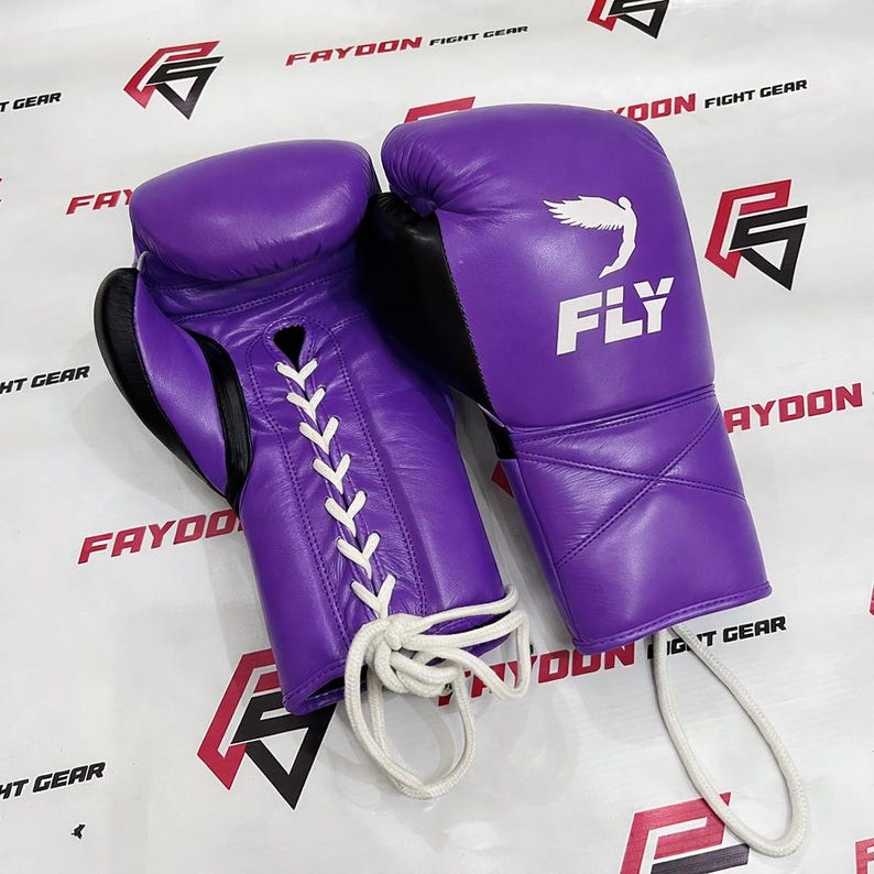May include: A pair of purple boxing gloves with black detailing. The gloves feature white laces and the word "FLY" with a wing graphic on the wrist. These leather gloves are designed for combat sports and training.