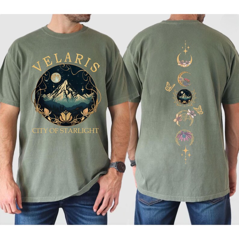 May include: Sage green t-shirt with a front graphic featuring a mountain scene within a circular frame, the word "VELARIS" and "CITY OF STARLIGHT". The back of the shirt displays moon phases and butterflies.
