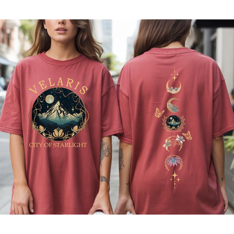 May include: A maroon t-shirt with the text "VELARIS CITY OF STARLIGHT" and a circular graphic of a mountain, moon, and stars. The back of the shirt features a design of moon phases, butterflies, and floral elements.