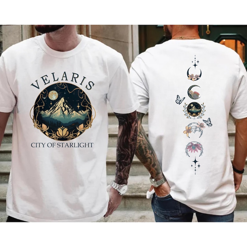 May include: White t-shirts with a graphic design. One shirt features the text "VELARIS CITY OF STARLIGHT" with a mountain and moon design. The other shirt has a design of moon phases and butterflies.