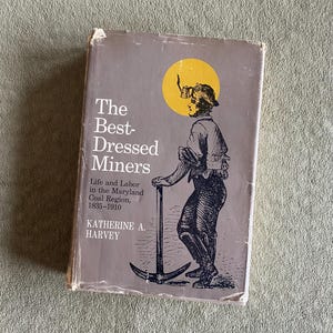 May include: A vintage book titled "The Best-Dressed Miners" with a gray cover. The cover features a black and white illustration of a miner holding a pickaxe, set against a yellow circle. The book's title and author's name are printed in white.